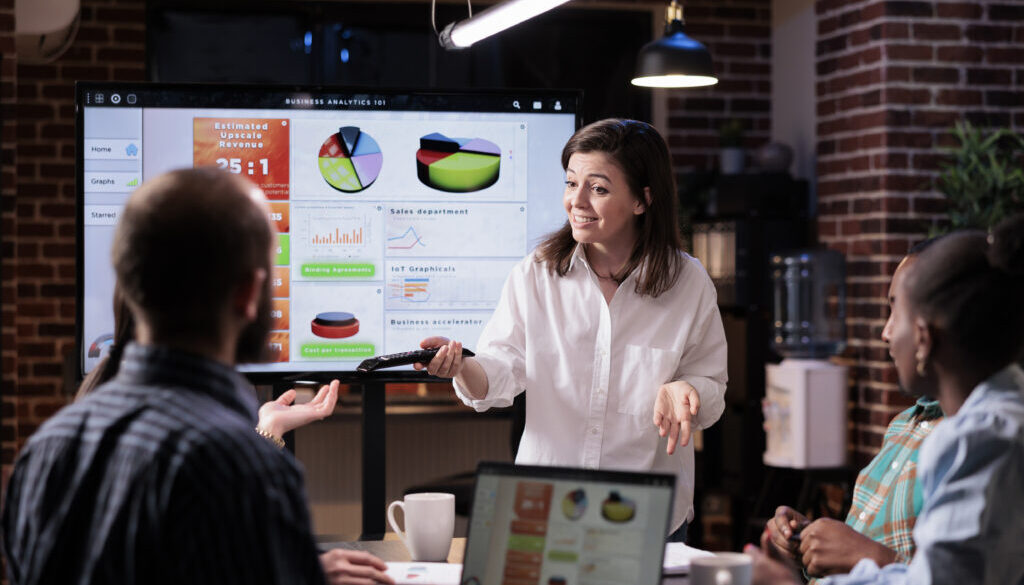 Smiling caucasian woman in startup office doing business presentation on big tv screen with charts