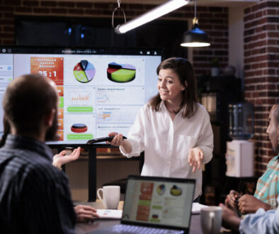 Smiling caucasian woman in startup office doing business presentation on big tv screen with charts