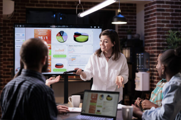 Smiling caucasian woman in startup office doing business presentation on big tv screen with charts